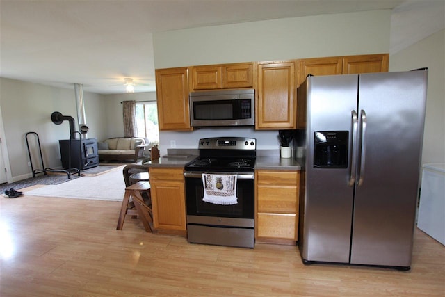 4155 Welsch Rd, Petoskey, MI 49770 - kitchen featuring stainless steel appliances, dark countertops, a wood stove, and light wood-style flooring
