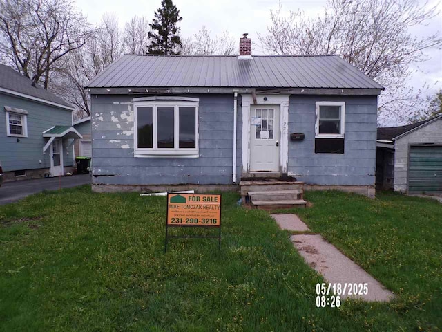 bungalow featuring metal roof, a chimney, and a front lawn
