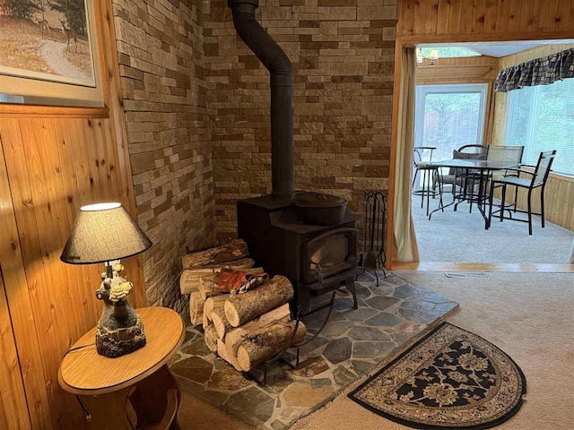15500 Riverside Trl, Wolverine, MI 49799 - living room featuring a wood stove, carpet flooring, wood walls, and brick wall