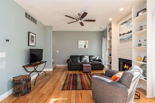 1766 Chippewa Bch, Indian River, MI 49749 - living room with a ceiling fan, light wood-style flooring, a glass covered fireplace, a textured ceiling, and built in features