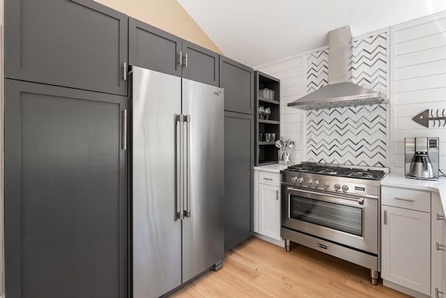 2018 Greenbriar Ter, Harbor Springs, MI 49740 - kitchen featuring high end appliances, wall chimney exhaust hood, lofted ceiling, tasteful backsplash, and light countertops