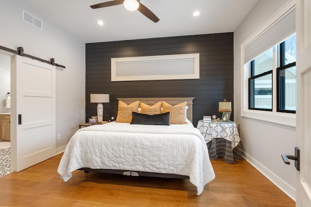 917 Grove St, Petoskey, MI 49770 - bedroom with a barn door, wood finished floors, recessed lighting, baseboards, and wood walls