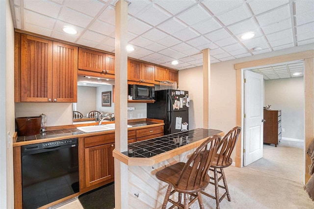 9030 Sugar Tree Ln, Charlevoix, MI 49720 - kitchen with black appliances, tile counters, a breakfast bar, brown cabinetry, and recessed lighting