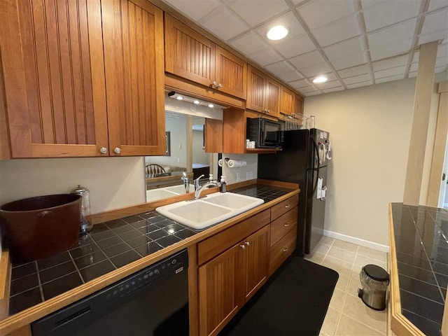 9030 Sugar Tree Ln, Charlevoix, MI 49720 - kitchen with black appliances, tile countertops, a sink, brown cabinetry, and light tile patterned floors