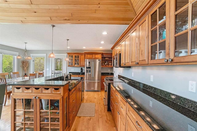 9030 Sugar Tree Ln, Charlevoix, MI 49720 - kitchen featuring appliances with stainless steel finishes, brown cabinetry, a sink, light wood-type flooring, and a kitchen island with sink