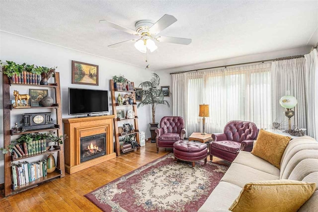6073 Rocky Beach Ave, Charlevoix, MI 49720 - living room featuring hardwood / wood-style flooring, a glass covered fireplace, a ceiling fan, and a textured ceiling