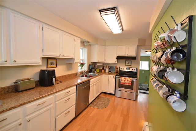 413 E Main St, Boyne City, MI 49712 - kitchen featuring appliances with stainless steel finishes, under cabinet range hood, a sink, white cabinetry, and light wood-type flooring