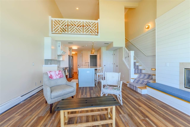 301 Michigan Ave Unit 13, Charlevoix, MI 49720 - living room featuring a high ceiling, baseboard heating, wood finished floors, stairs, and a fireplace with raised hearth
