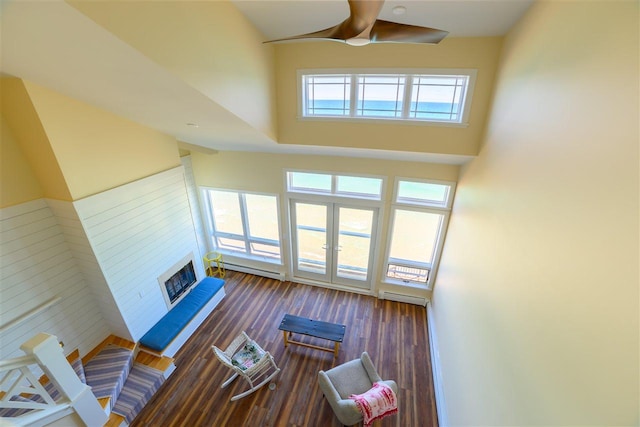 301 Michigan Ave Unit 13, Charlevoix, MI 49720 - living room with a fireplace with raised hearth, a ceiling fan, a baseboard radiator, a high ceiling, and wood finished floors