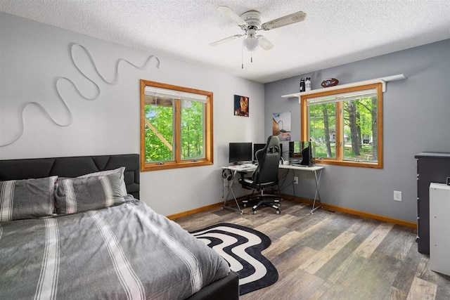 10370 Boyne City Rd, Charlevoix, MI 49720 - bedroom with wood finished floors, baseboards, a textured ceiling, an office area, and a ceiling fan