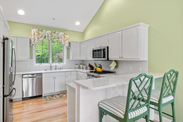 6707 Cottage Ct Unit 40, Bay Harbor, MI 49770 - kitchen with appliances with stainless steel finishes, a peninsula, light wood-style floors, decorative backsplash, and a kitchen breakfast bar