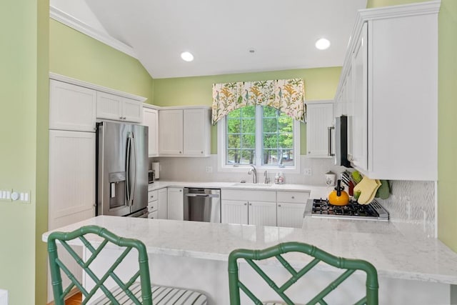 6707 Cottage Ct Unit 40, Bay Harbor, MI 49770 - kitchen featuring appliances with stainless steel finishes, a peninsula, decorative backsplash, a breakfast bar area, and vaulted ceiling