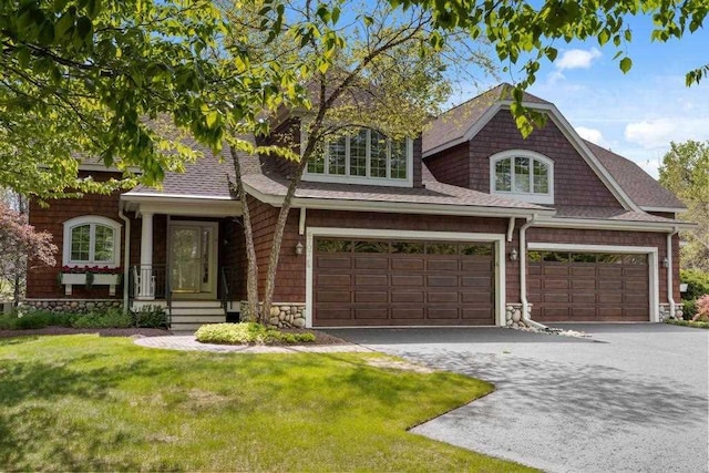 6707 Cottage Ct Unit 40, Bay Harbor, MI 49770 - view of front of property with a front yard, a garage, driveway, stone siding, and a shingled roof