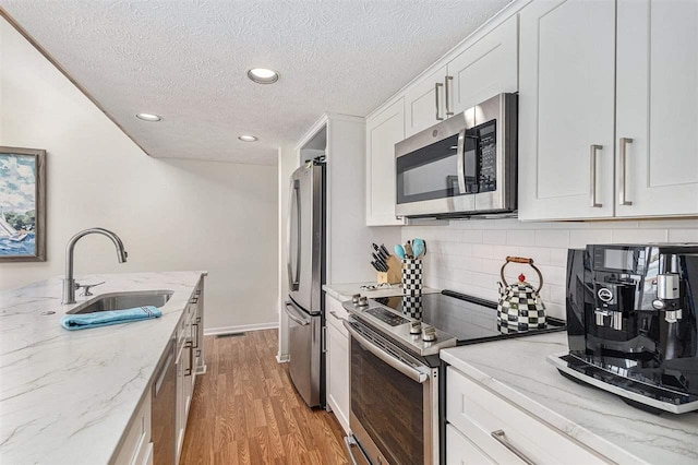 3480 Lakeside Dr N Unit 35, Petoskey, MI 49770 - kitchen featuring appliances with stainless steel finishes, a sink, light wood-style floors, tasteful backsplash, and white cabinets