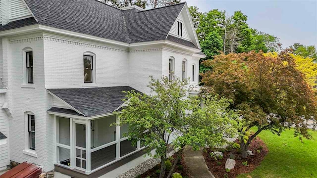 503 N Bridge St, Bellaire, MI 49615 - view of property exterior featuring roof with shingles, brick siding, and a sunroom
