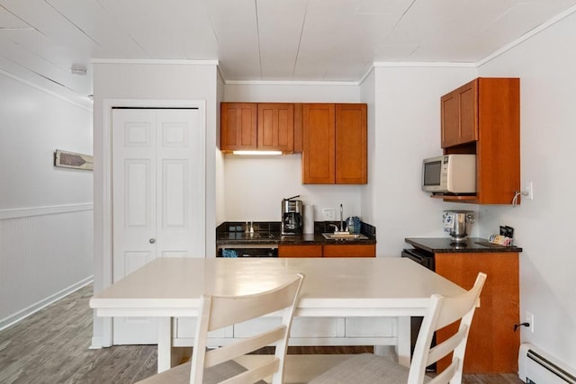 101 Michigan Ave Unit 107, Charlevoix, MI 49720 - kitchen with white microwave, baseboard heating, brown cabinetry, crown molding, and wood finished floors