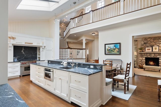 145 Traverse St, Harbor Springs, MI 49740 - kitchen featuring dark wood-style flooring, a towering ceiling, white cabinetry, a stone fireplace, and a center island with sink