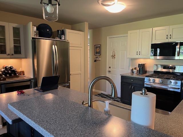 700 Fairways Dr Unit 14, Harbor Springs, MI 49740 - kitchen featuring stainless steel appliances, dark countertops, white cabinets, and glass insert cabinets