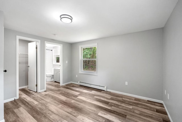 3049 Chippewa Beach Rd, Indian River, MI 49749 - unfurnished bedroom with baseboard heating, light wood-style flooring, a walk in closet, and a closet