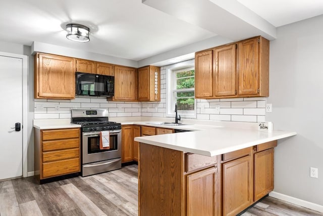 3049 Chippewa Beach Rd, Indian River, MI 49749 - kitchen with black microwave, stainless steel gas range, a peninsula, tasteful backsplash, and light wood finished floors
