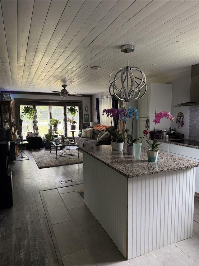 6515 Pincherry Rd, Charlevoix, MI 49720 - kitchen featuring wall chimney exhaust hood, open floor plan, a kitchen island, a chandelier, and dark stone countertops