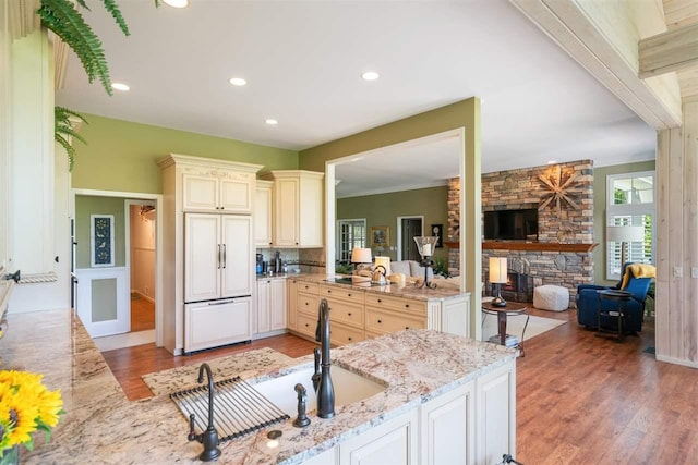 690 Woodhill Unit 6, Harbor Springs, MI 49740 - kitchen with paneled fridge, cream cabinets, light wood-style floors, a fireplace, and light stone counters