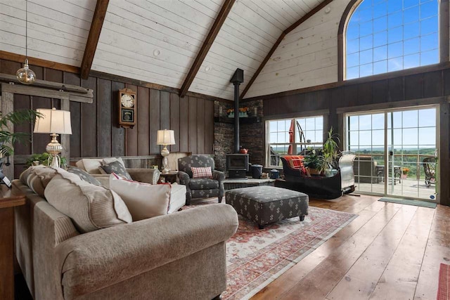 9235 Bailey Rd, East Jordan, MI 49727 - living area with a wood stove, wood-type flooring, high vaulted ceiling, wooden walls, and a wood ceiling with exposed beams