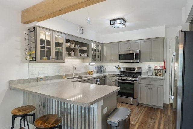 1185 Hideaway Valley Dr Unit 60, Harbor Springs, MI 49740 - kitchen with stainless steel appliances, a peninsula, decorative backsplash, a kitchen bar, and gray cabinetry