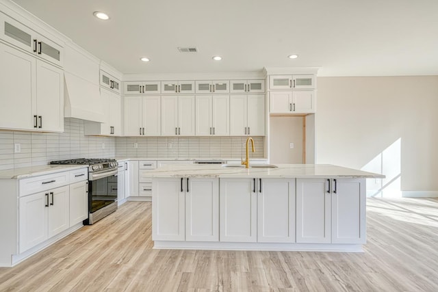 155 Chestnut Dr, Woodruff, SC 29388 - kitchen featuring stainless steel gas range, an island with sink, decorative backsplash, light wood-style flooring, and light stone countertops