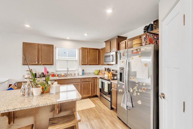 2068 Wexley Dr, Boiling Springs, SC 29316 - kitchen with stainless steel appliances, brown cabinets, a kitchen bar, light wood-style flooring, and light stone countertops