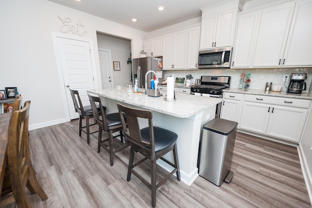 637 Grays Creek Rd, Spartanburg, SC 29303 - kitchen with stainless steel appliances, a kitchen island with sink, white cabinetry, light wood finished floors, and decorative backsplash
