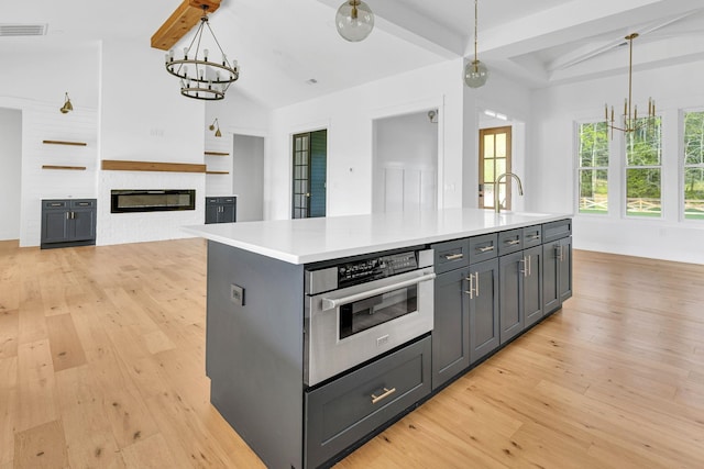 164 Triangle Pine Rd, Fountain Inn, SC 29644 - kitchen with light wood-style flooring, an island with sink, light countertops, and a glass covered fireplace