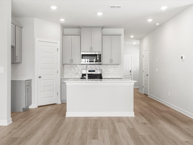 126 Arrow Ct, Greer, SC 29651 - kitchen featuring stainless steel appliances, gray cabinetry, a center island with sink, decorative backsplash, and light wood-style flooring