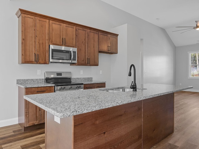 1328 Shoresbrook Rd, Spartanburg, SC 29301 - kitchen featuring appliances with stainless steel finishes, brown cabinets, wood finished floors, vaulted ceiling, and light stone counters