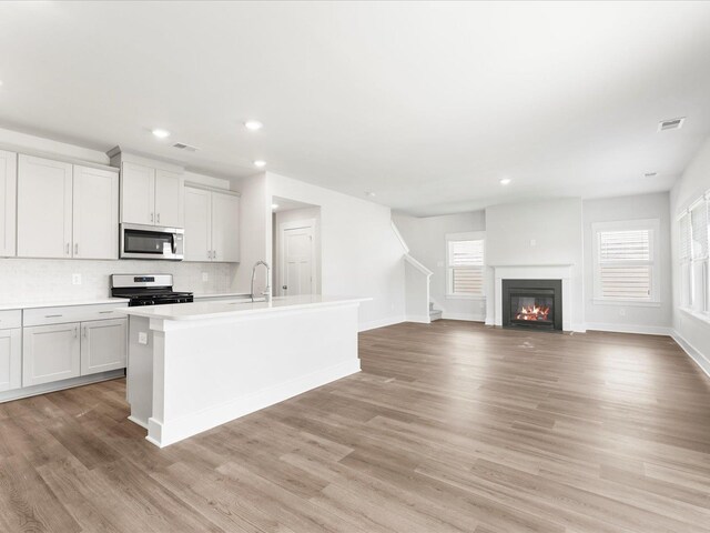791 Burghley Cir, Greer, SC 29651 - kitchen with stainless steel microwave, range with electric cooktop, tasteful backsplash, an island with sink, and light countertops
