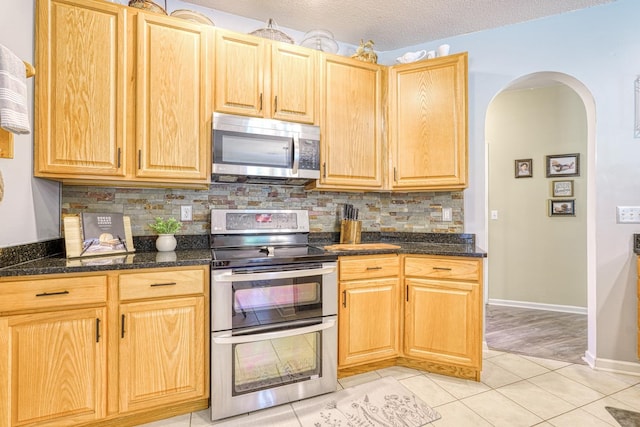 316 Crestview Ln, Spartanburg, SC 29301 - kitchen featuring stainless steel appliances, backsplash, arched walkways, light tile patterned floors, and dark stone countertops