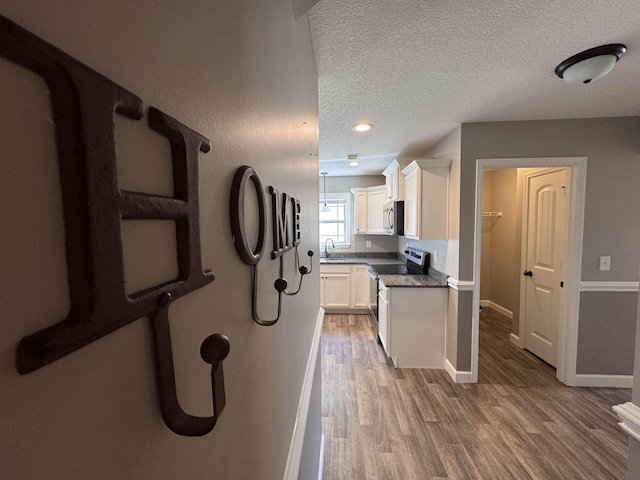 313 Trail Crossing Ln, Inmann, SC 29349 - kitchen featuring appliances with stainless steel finishes, light wood-style flooring, white cabinetry, dark countertops, and a textured ceiling
