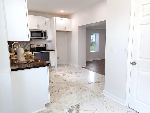 2115 Oakhurst Cir, Spartanburg, SC 29302 - kitchen with stainless steel appliances, dark countertops, white cabinets, light marble finish floors, and backsplash