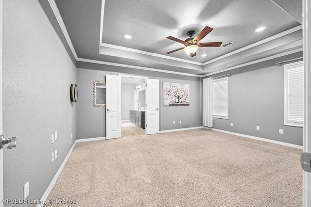 unfurnished bedroom featuring light carpet, a tray ceiling, ceiling fan, crown molding, and connected bathroom