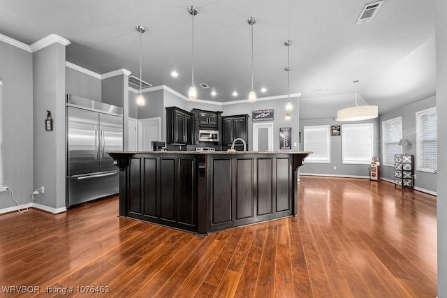 kitchen featuring pendant lighting, dark wood-type flooring, a large island with sink, appliances with stainless steel finishes, and stone countertops