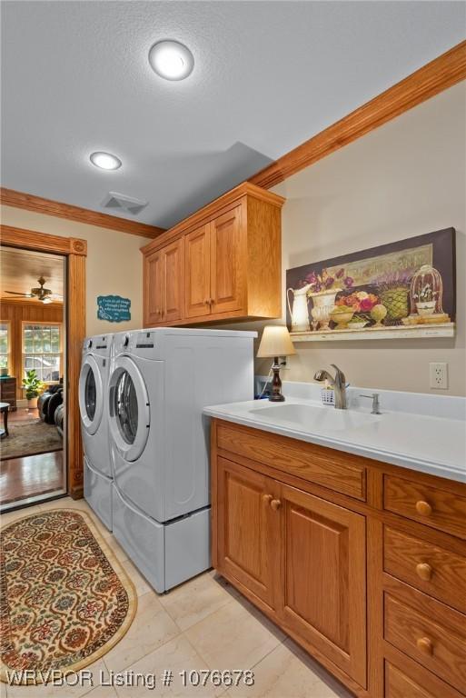 clothes washing area with separate washer and dryer, crown molding, sink, and cabinets