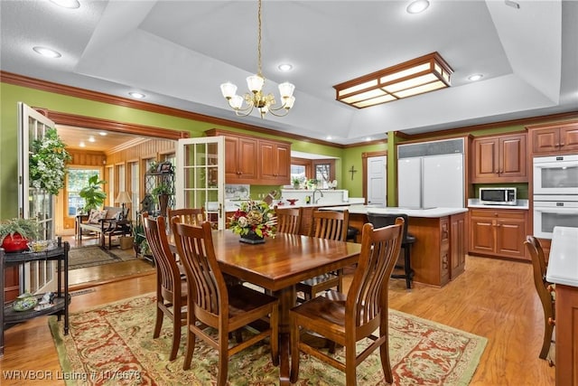 dining area featuring ornamental molding, light wood-type flooring, a tray ceiling, and a notable chandelier