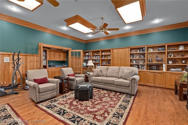 living room featuring ceiling fan, wood walls, light wood-type flooring, and ornamental molding