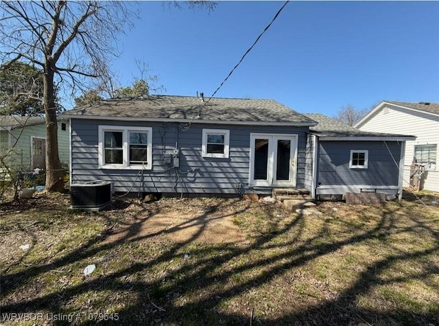 rear view of house with a shingled roof, fence, entry steps, central AC unit, and a yard