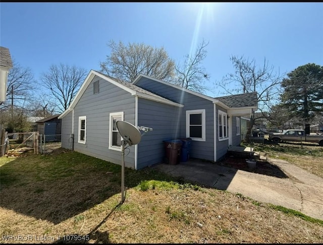 view of side of home with a gate, roof with shingles, a yard, and fence