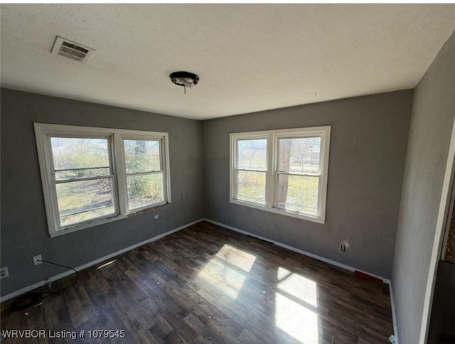 spare room featuring visible vents, plenty of natural light, baseboards, and dark wood finished floors