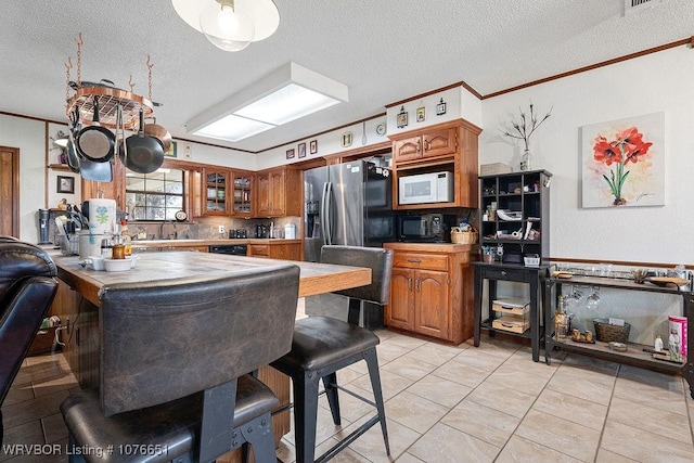 kitchen featuring light tile patterned flooring, sink, stainless steel fridge, ornamental molding, and a textured ceiling