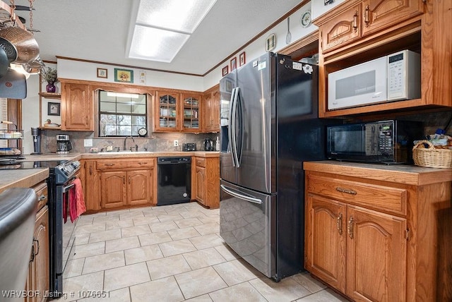 kitchen featuring sink, crown molding, black appliances, light tile patterned flooring, and decorative backsplash