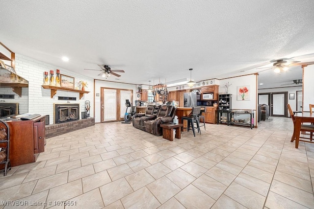 living room featuring ceiling fan, a brick fireplace, and a textured ceiling