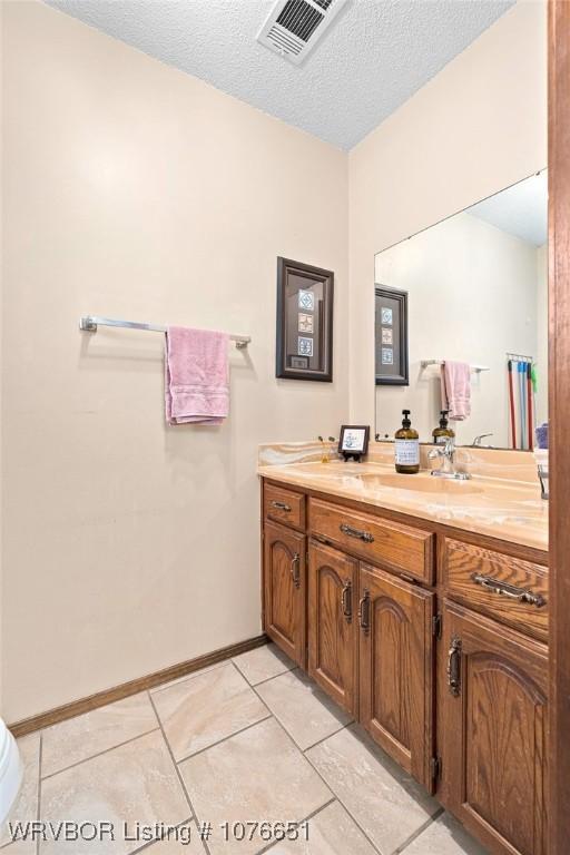 bathroom with tile patterned flooring, vanity, toilet, and a textured ceiling